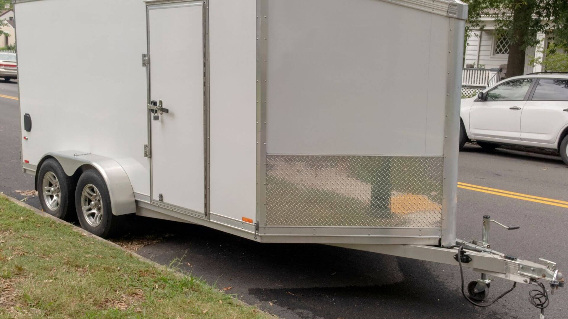 White enclosed cargo trailer parked roadside with tandem axles and front access door